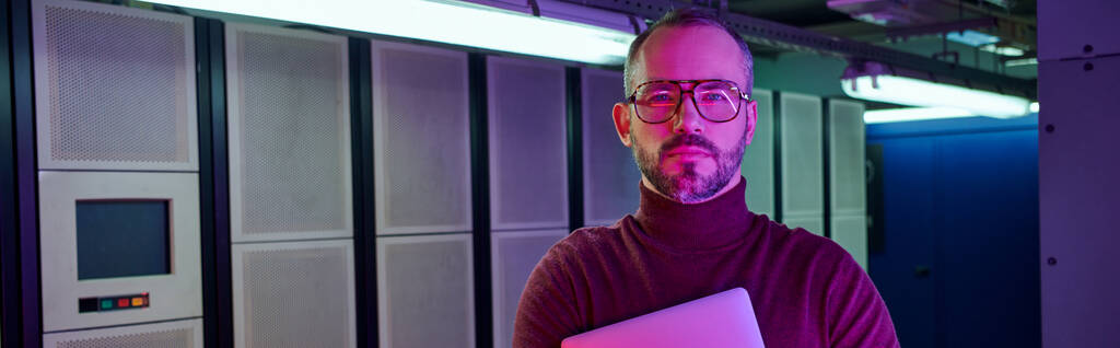 pensive specialist in turtleneck holding laptop and looking at camera, data center, banner - Photo, Image