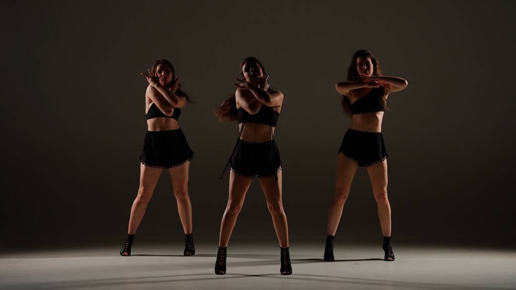 Grupo de mulheres dançando saltos dança em um estúdio. Fundo sombreado, holofotes. Traje sexy preto, saltos altos. Coreografia sensual moderna. Comprimento total. Clipe promocional ou propaganda. - Foto, Imagem