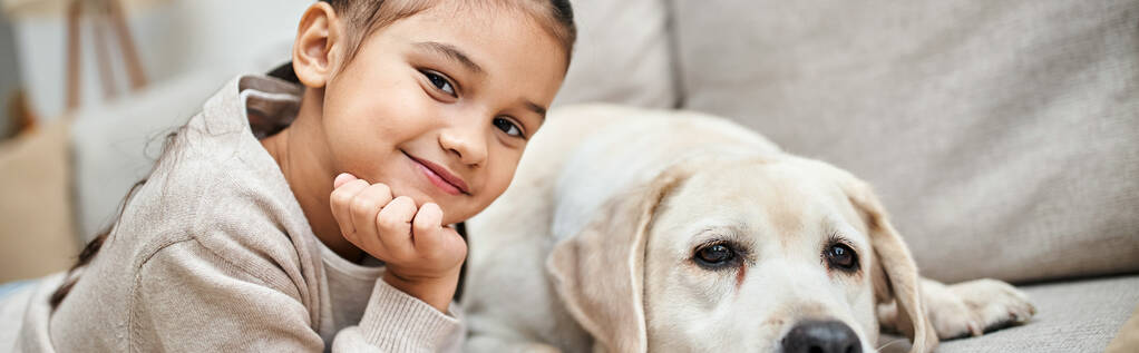 retrato de niña feliz sonriendo cerca lindo labrador en sala de estar moderna, mascota con bandera de niño - Foto, Imagen