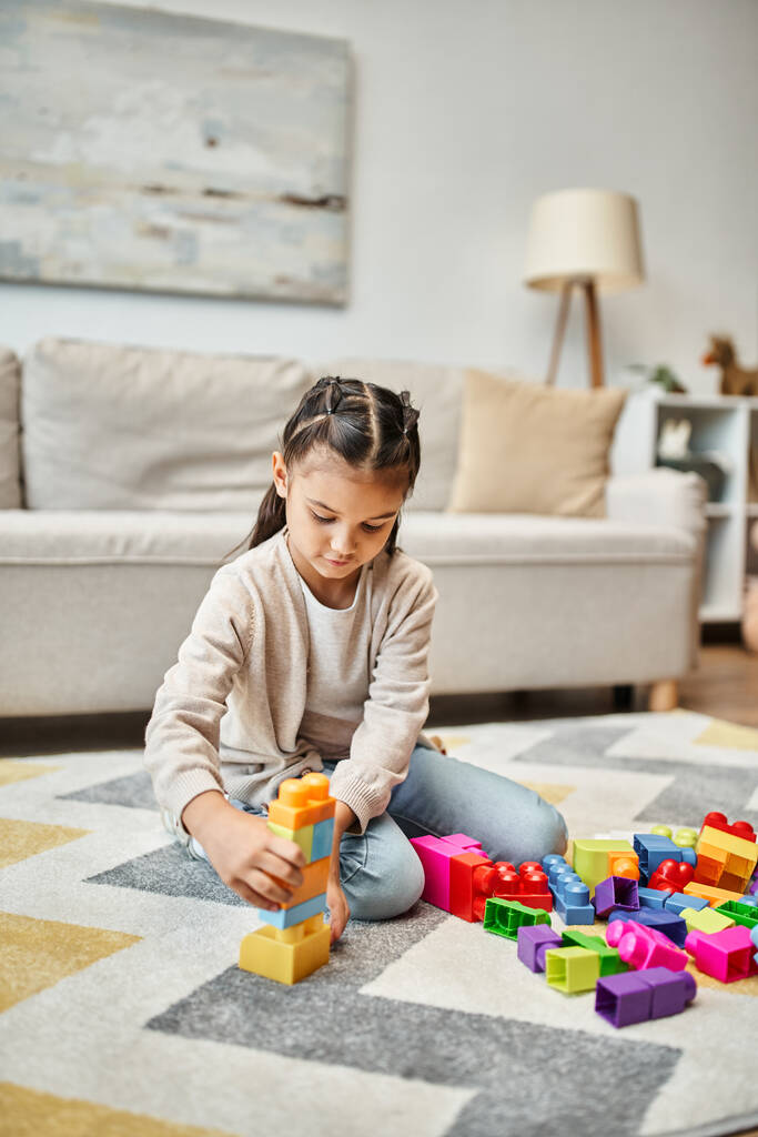 Mädchen im Grundalter spielen mit bunten Spielzeugklötzen auf Teppich im Wohnzimmer, Turmbau-Spiel - Foto, Bild