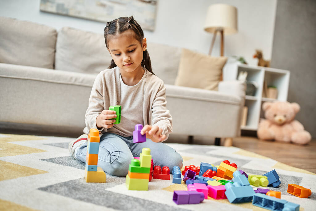 リビングルームのカーペットのカラフルなおもちゃブロックで遊ぶかわいい小さな女の子,ビルディングタワーゲーム - 写真・画像