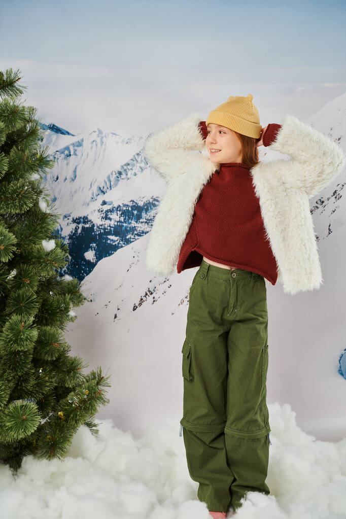 весела дівчина в стильному зимовому вбранні позує руками за голову і дивиться в сторону, мода - Фото, зображення