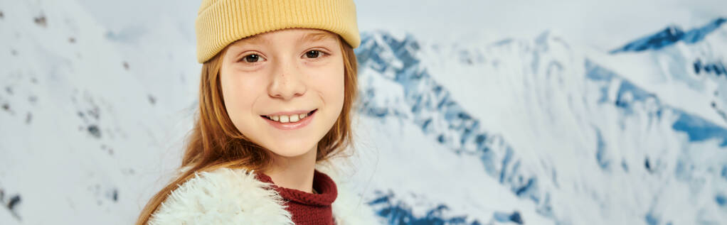 niña de moda en traje cálido y elegante sonriendo a la cámara con telón de fondo de montaña, moda, pancarta - Foto, imagen