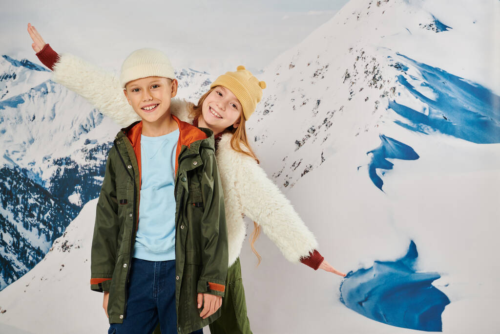 fröhliche kleine Jungen und Mädchen mit Mützen haben Spaß mit schneebedeckten Berg auf der Kulisse, Mode - Foto, Bild