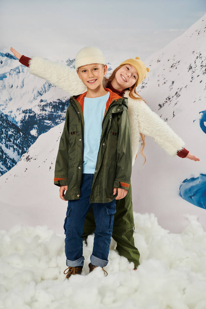 vertikale Aufnahme von kleinen netten Freunden in Winterkleidung, die zusammen posieren und Spaß haben, Mode - Foto, Bild