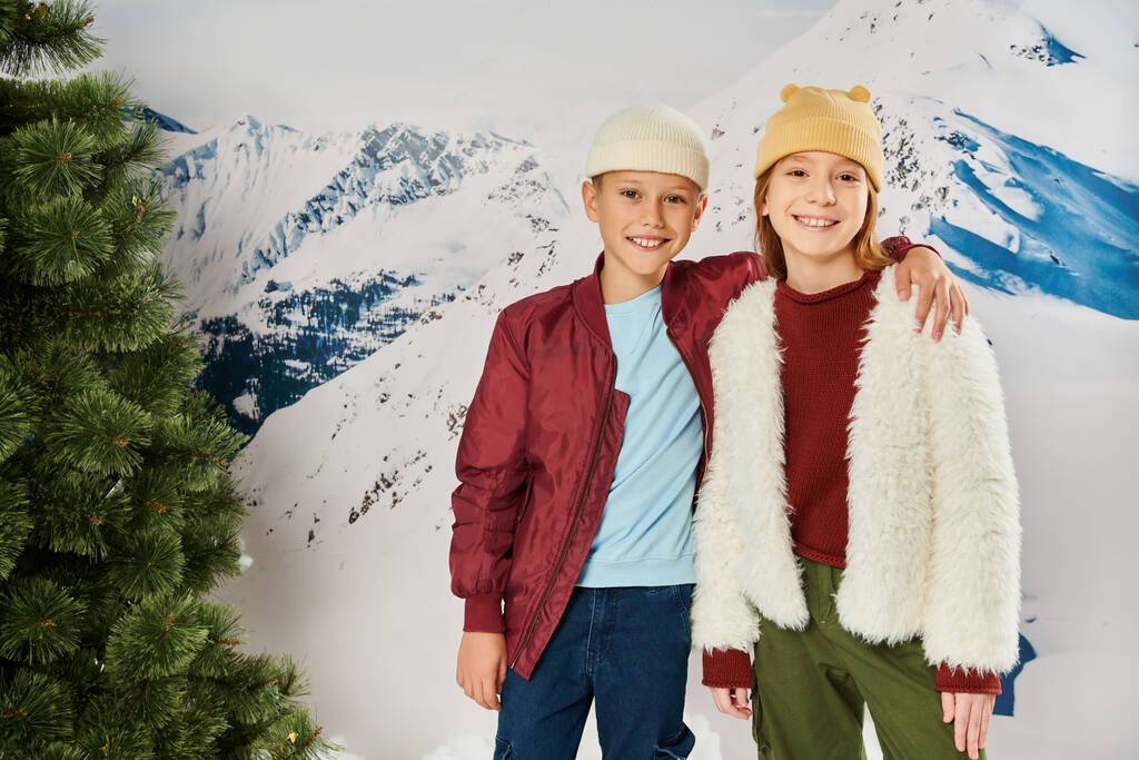 niño pequeño con la mano en el hombro de la chica sonriendo a la cámara, traje de invierno con estilo, concepto de moda - Foto, Imagen