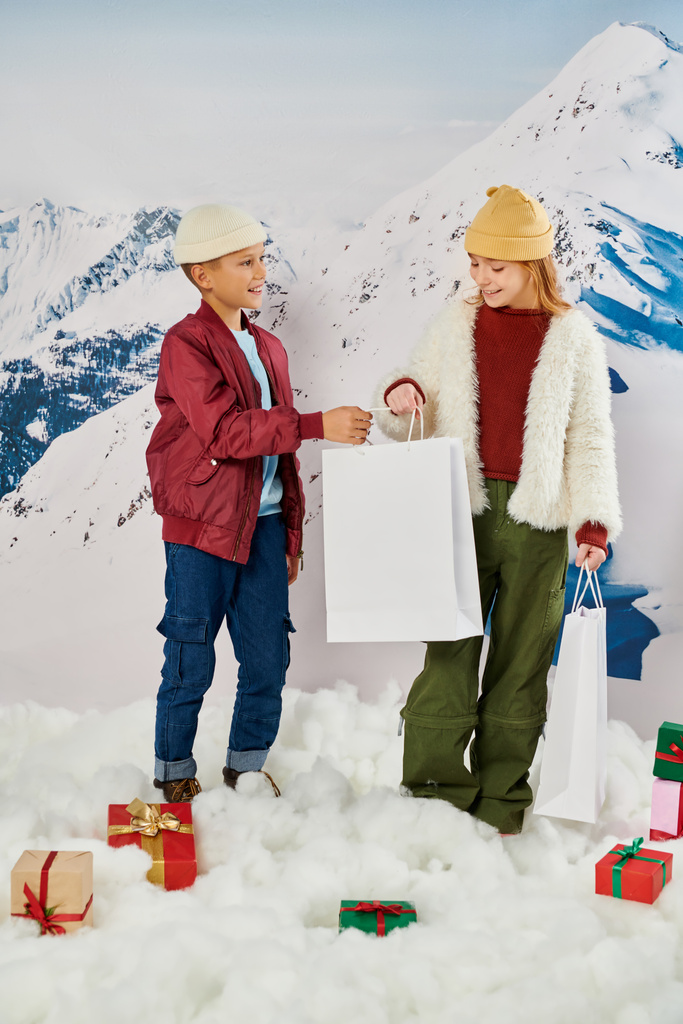 lustiger preteen boy schenkt geschenktüte an kleines mädchen umgeben von geschenken auf schnee, modekonzept - Foto, Bild