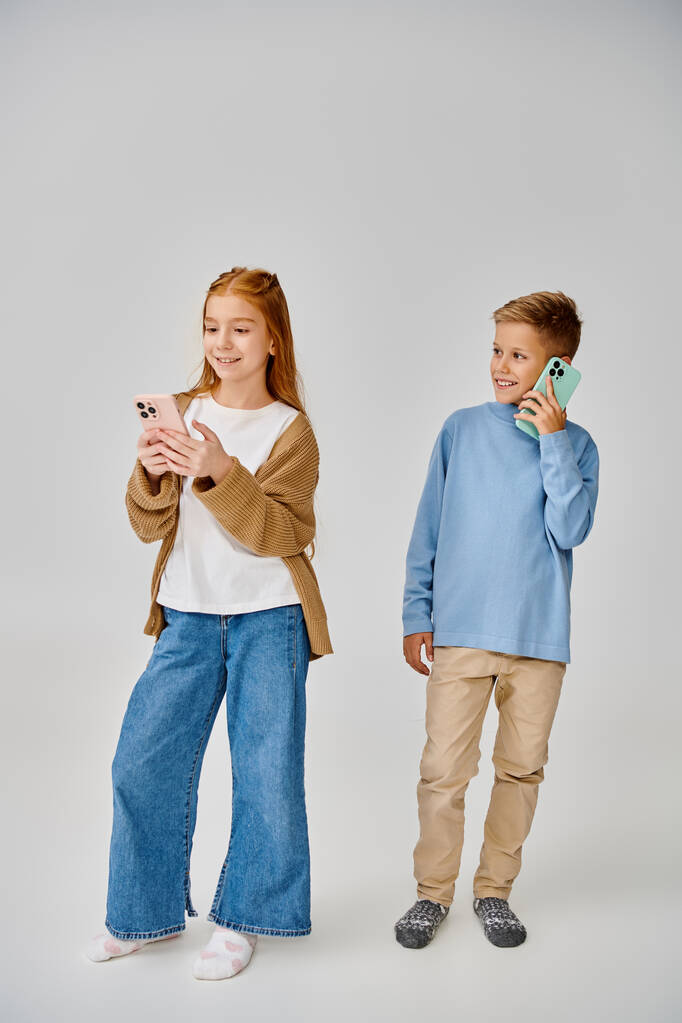 вертикальный снимок веселых юных друзей в теплых модных нарядах, позирующих с телефонами, мода - Фото, изображение