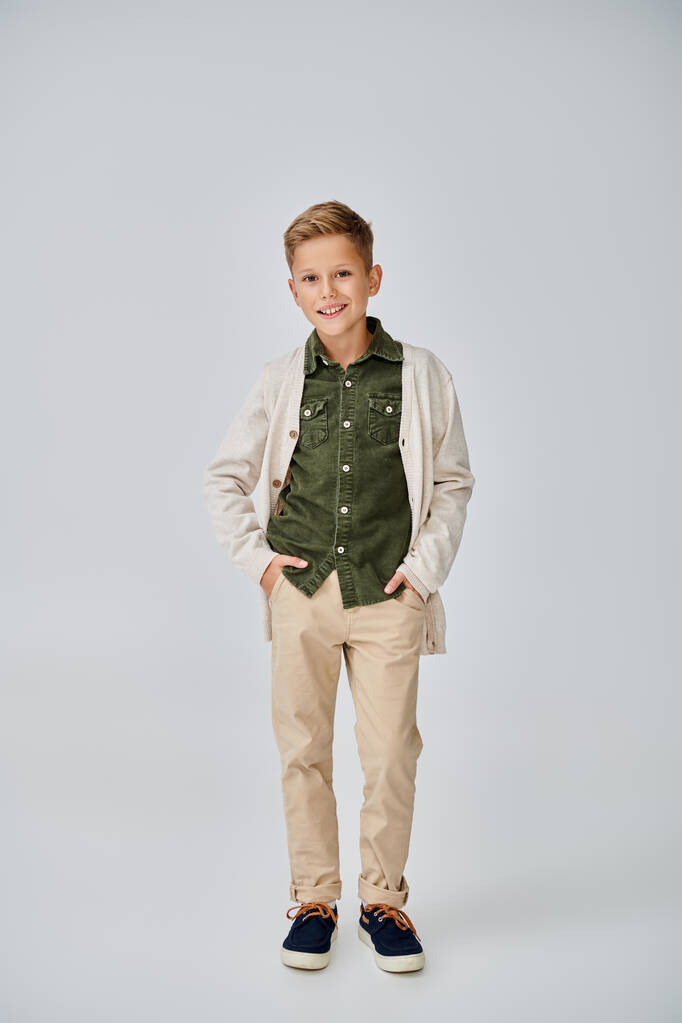 tiro vertical de menino pré-adolescente em roupa casual em pano de fundo cinza com as mãos nos bolsos, moda - Foto, Imagem