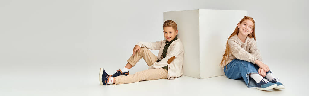 jolly little friends sitting on floor next to white cube smiling at camera, fashion concept, banner - Photo, Image