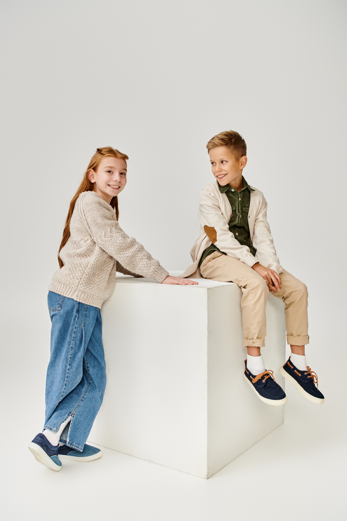 cheerful little boy in cardigan smiling at preteen red haired girl that looking at camera, fashion - Photo, Image