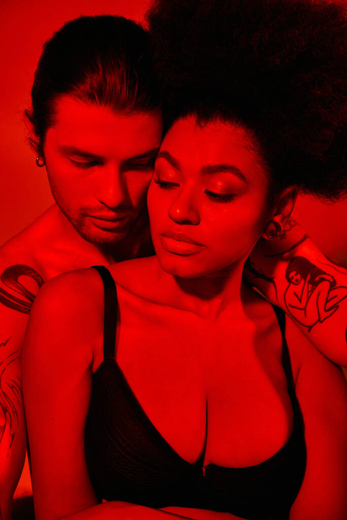 hombre guapo con tatuajes posando con su novia afroamericana en sujetador negro, sexy pareja - Foto, Imagen