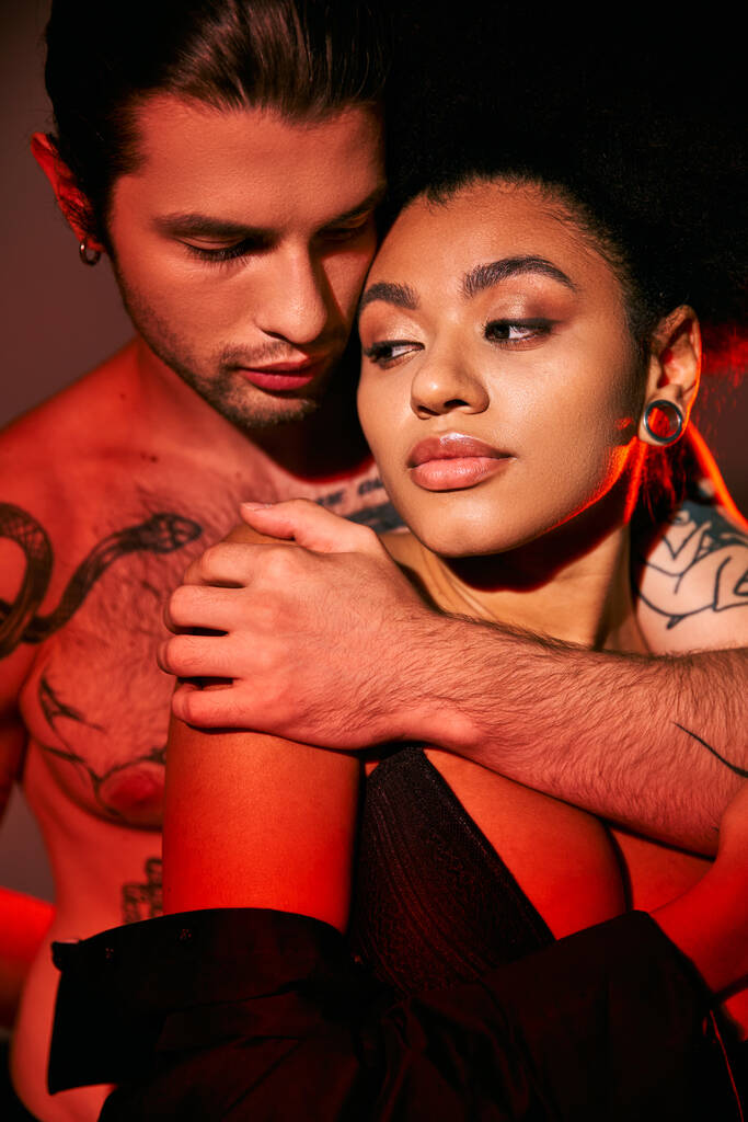 Yakışıklı dövmeli adam Afrikalı Amerikalı sevgilisine arkadan sarılıyor, seksi çift. - Fotoğraf, Görsel