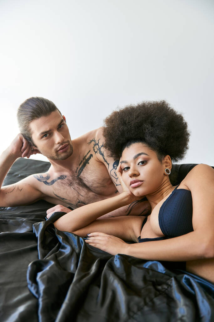 schöner Mann schaut in die Kamera und liegt mit seiner schönen afrikanisch-amerikanischen Freundin im Bett - Foto, Bild