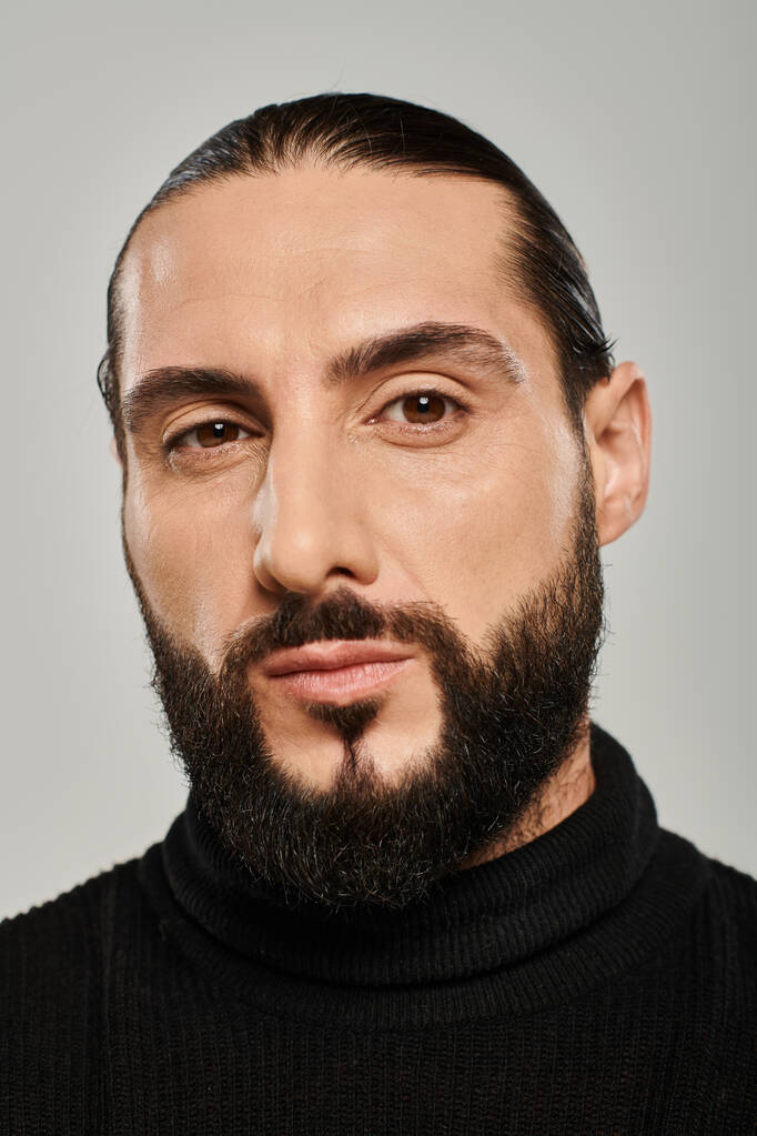 Porträt eines männlichen arabischen Mannes mit Bart, der in schwarzem Rollkragen auf grauem Hintergrund posiert - Foto, Bild
