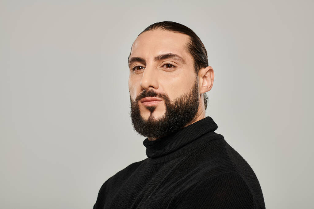 portrait of bearded and masculine arabic man posing in black turtleneck on grey background - Photo, Image