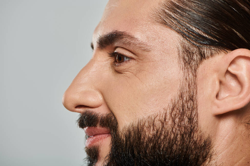 profil veselého arabského muže s vousy usmívající se a odvracející se na šedém pozadí - Fotografie, Obrázek