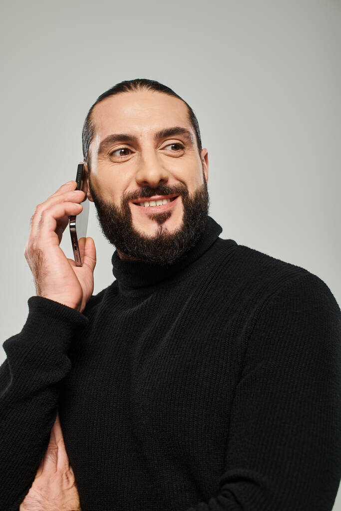 весёлый арабик с бородой улыбается и звонит по смартфону на сером фоне - Фото, изображение