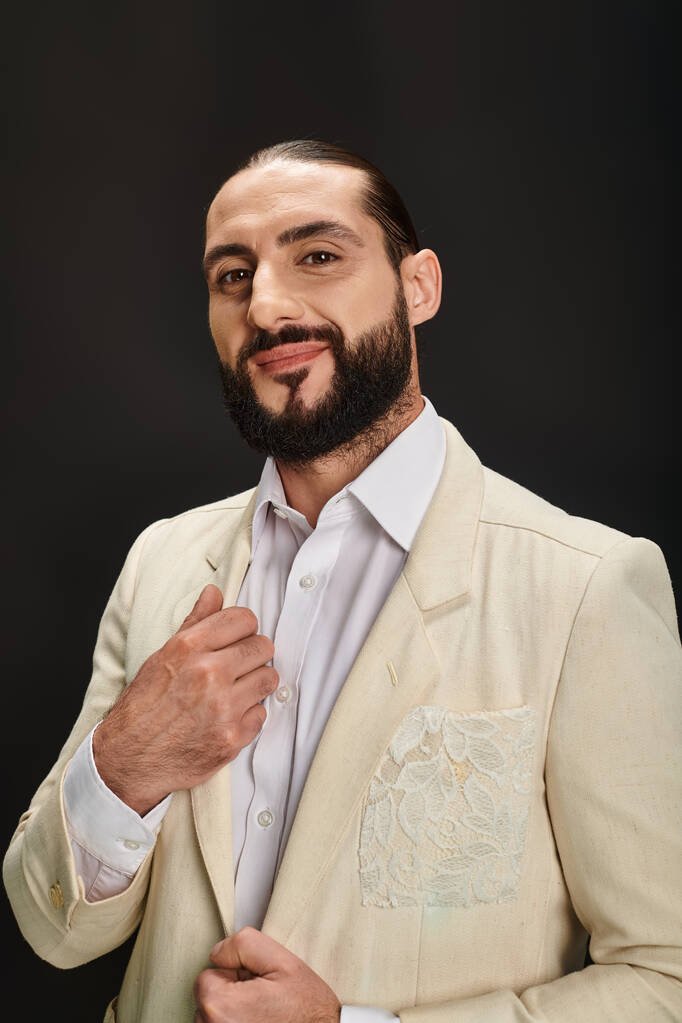 Beyaz gömlekli ve ceketli mutlu ve sakallı Arap adam siyah arka planda kameraya bakıyor. - Fotoğraf, Görsel