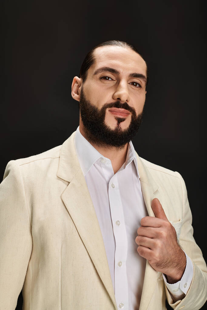 elegante e barbuto uomo arabo in camicia bianca e blazer guardando la fotocamera su sfondo nero - Foto, immagini