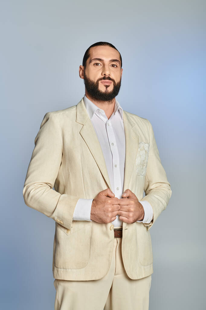 модный и бородатый мужчина в белой рубашке и блейзере позирует на сером фоне, элегантный наряд - Фото, изображение