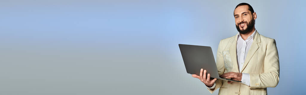 glücklicher bärtiger arabischer Mann in eleganter formaler Kleidung mit Laptop auf grauem Hintergrund, Banner des digitalen Zeitalters - Foto, Bild