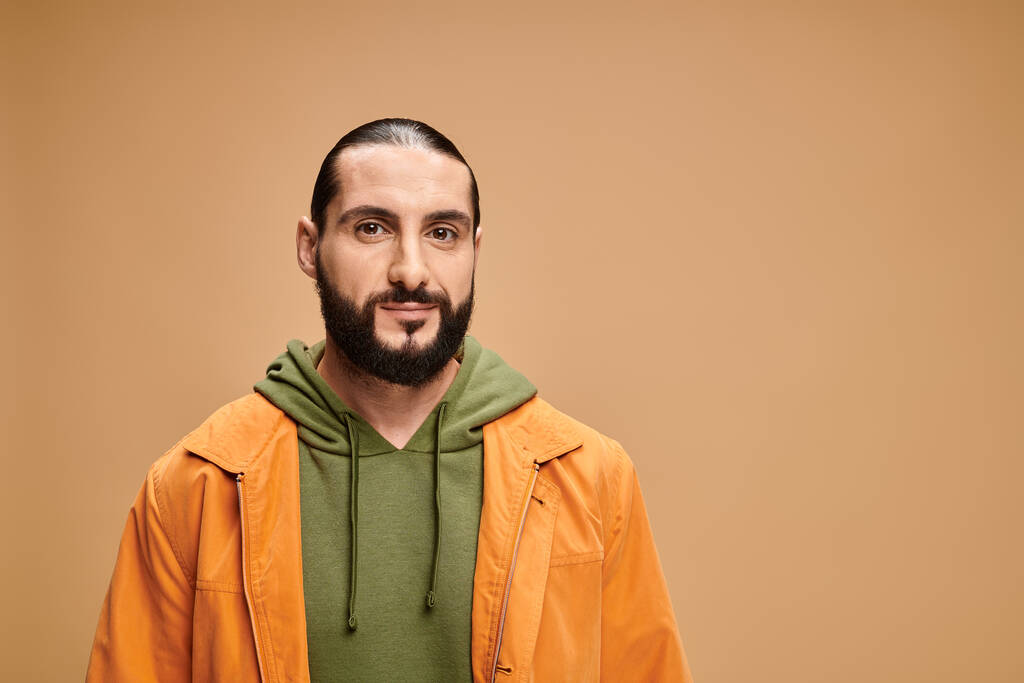 portret van knappe en bebaarde Arabische man in casual kleding kijkend naar camera op beige achtergrond - Foto, afbeelding