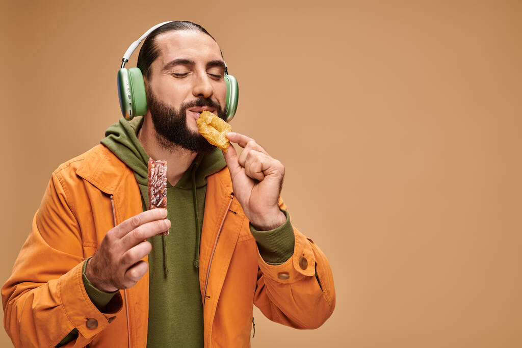 hombre alegre en auriculares comiendo delicioso baklava miel en fondo beige, delicias turcas - Foto, imagen