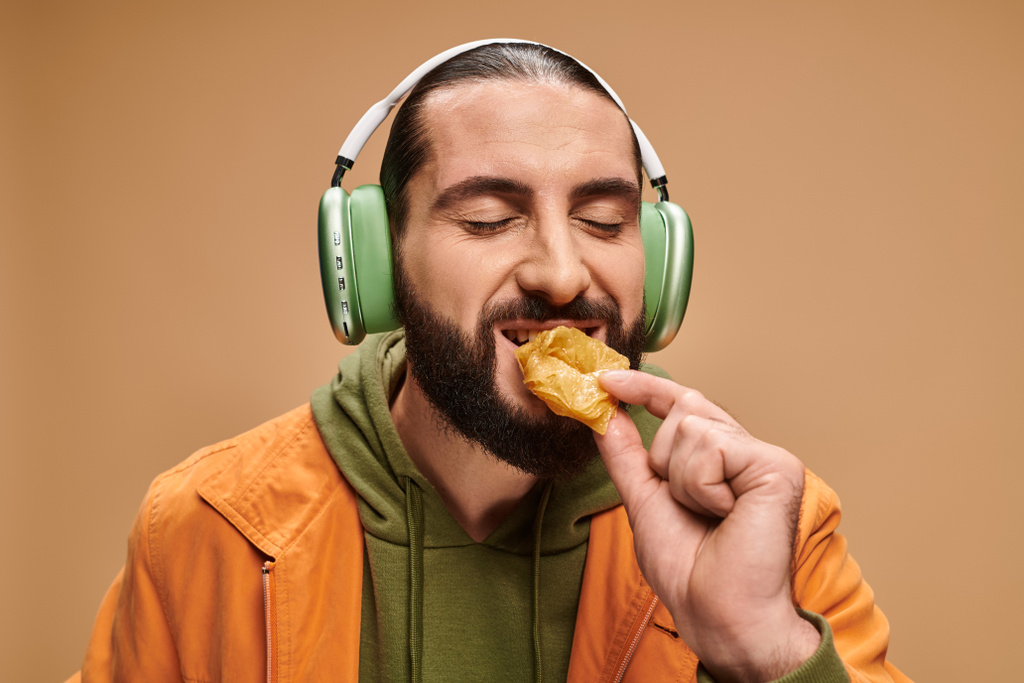 hombre alegre en auriculares comiendo delicioso baklava miel en fondo beige, delicias turcas - Foto, Imagen
