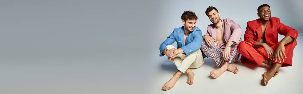 明るいスーツの陽気な多様な男性は,交差した足と笑顔で床に座って,バナー - 写真・画像