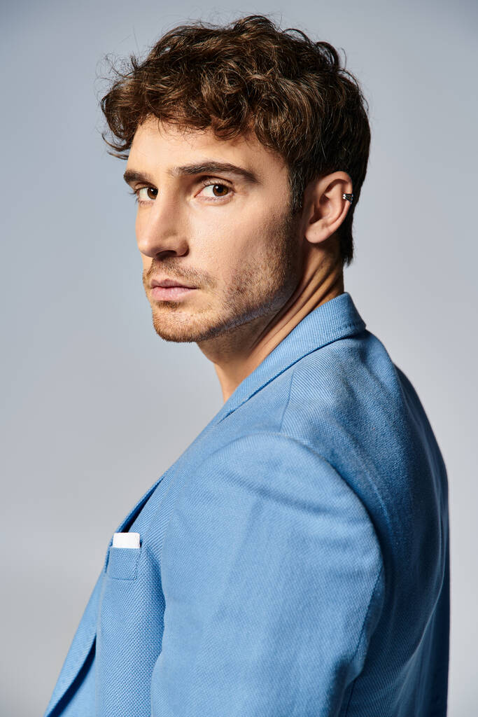 young good looking man in vibrant unbuttoned blue jacket posing on gray backdrop, fashion concept - Photo, Image
