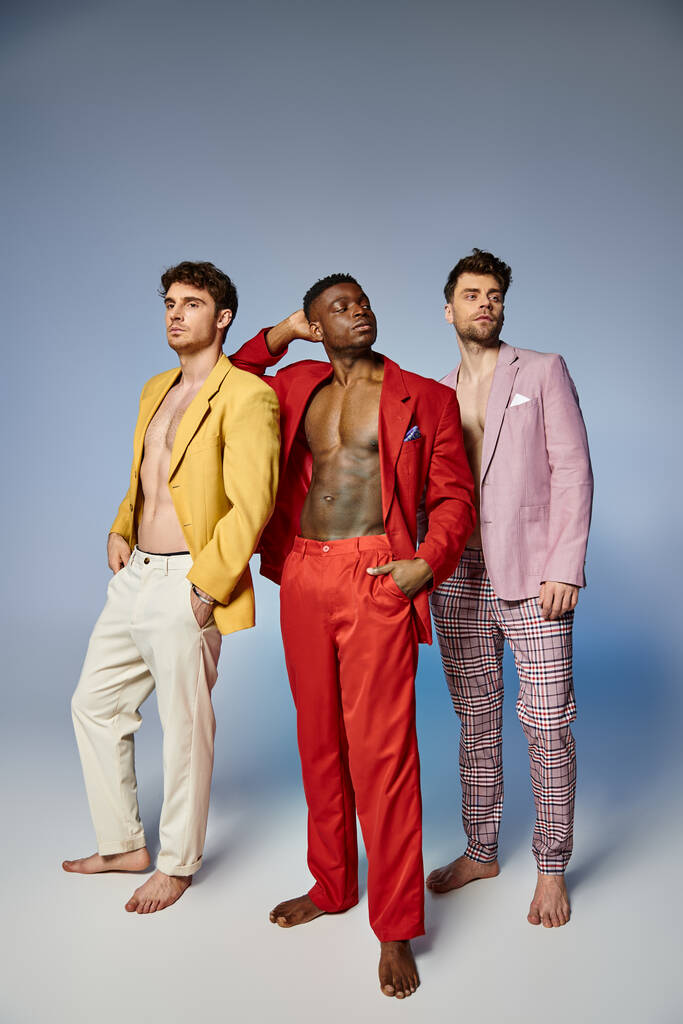 aantrekkelijk sexy diverse mannen in unbuttoned levendige pakken poseren op grijze achtergrond, mode concept - Foto, afbeelding