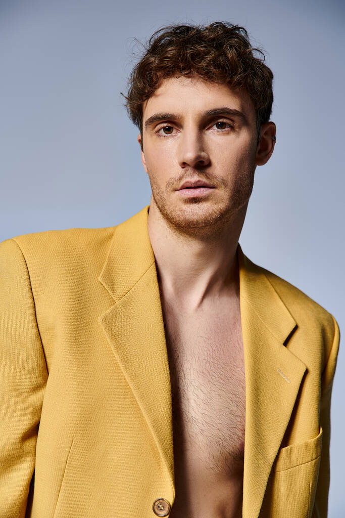 attraktiver junger Mann in trendiger gelber Jacke posiert attraktiv vor grauem Hintergrund, Modekonzept - Foto, Bild
