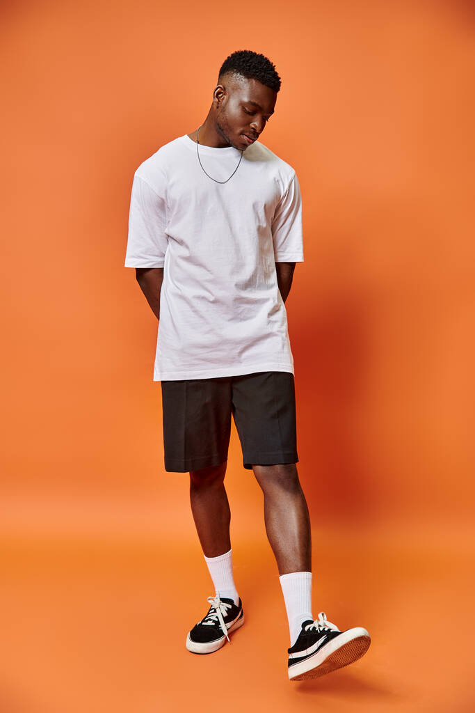 привлекательный молодой африканский американец в уличной повседневной одежде на оранжевом фоне, концепция моды - Фото, изображение