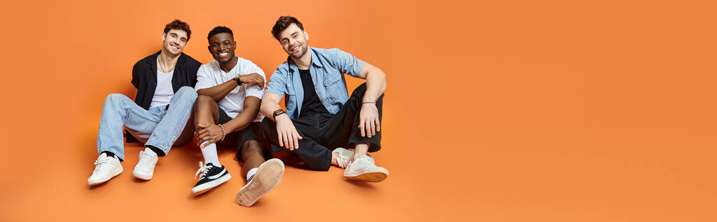three diverse happy men in casual clothes smiling and sitting on floor, fashion concept, banner - Photo, Image