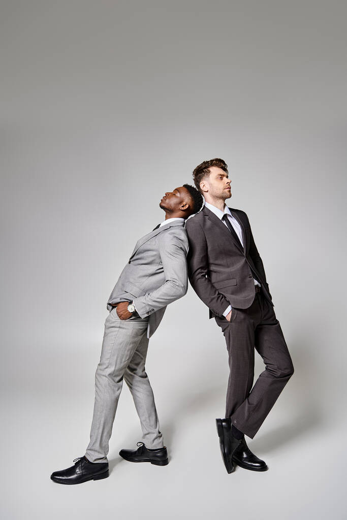 zwei hübsche trendige multikulturelle männliche Models in schicker Business-Kleidung posieren vor grauem Hintergrund - Foto, Bild