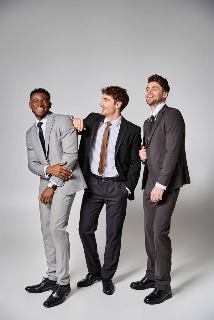 グレーの背景に誠実に微笑んでいるスマートなスーツの幸せな異人種間の男性モデル - 写真・画像