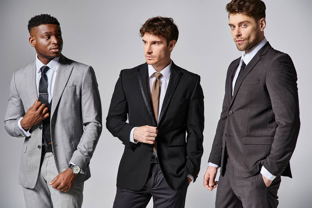 красивые стильные мультикультурные модели мужчин в бизнесе элегантные смарт-костюмы позировать на сером фоне - Фото, изображение