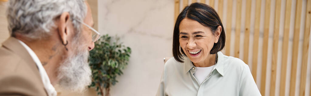 šťastná žena středního věku se usmívá poblíž vousaté realitní kancelář v realitní kanceláři, banner - Fotografie, Obrázek