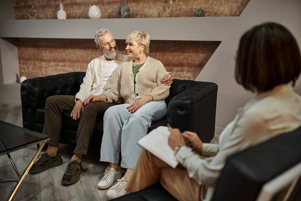 бородатый мужчина обнимает счастливую жену среднего возраста во время сеанса терапии с семейным психологом - Фото, изображение