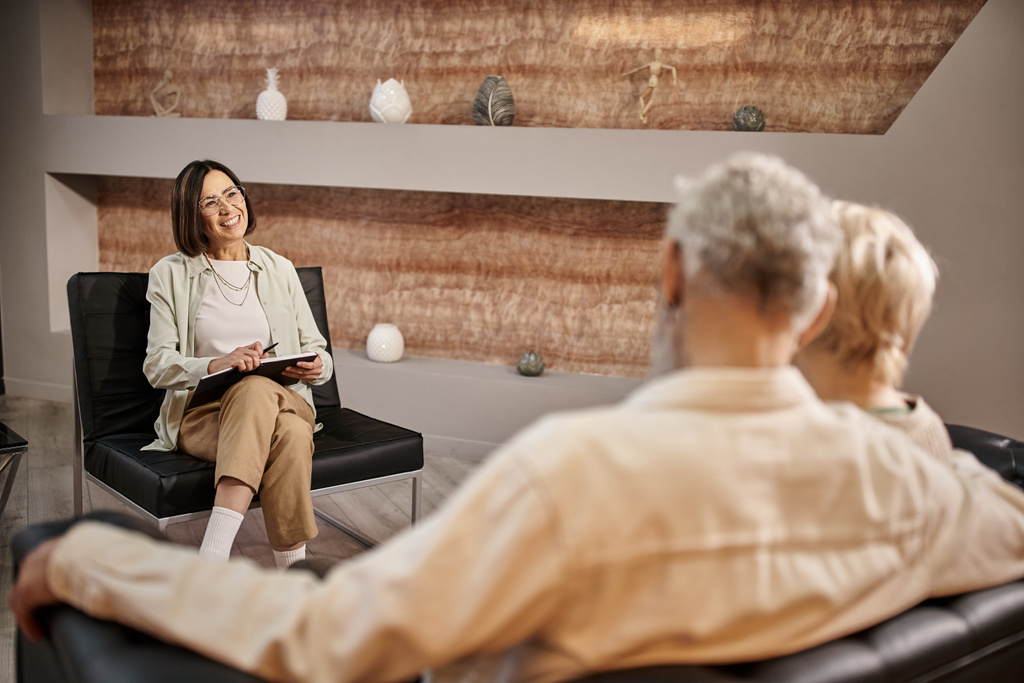 Psychologe mittleren Alters in Brille sitzt bei Familientherapiesitzung neben Ehepaar - Foto, Bild