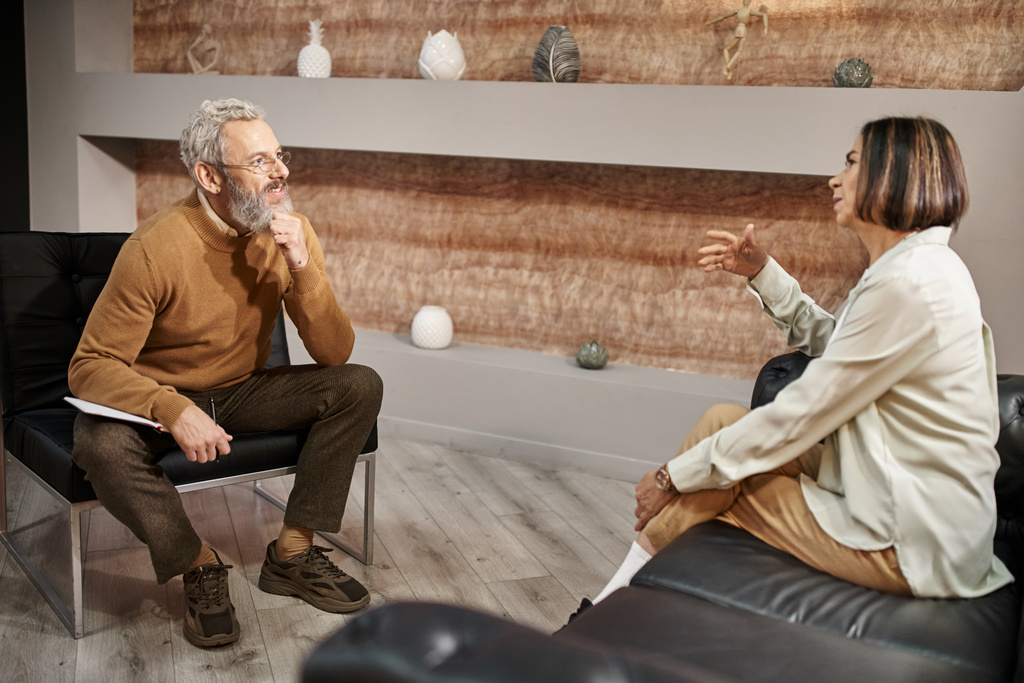 brodaty psycholog w średnim wieku w okularach rozmawiający z klientką podczas sesji terapeutycznej - Zdjęcie, obraz