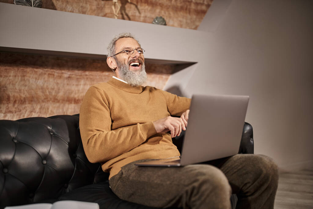 radosny psycholog w średnim wieku z brodą rozmawiający podczas konsultacji online z klientem na laptopie - Zdjęcie, obraz