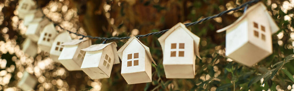 sztandar ekologicznej girlandy z drewnianych domów na zielonym drzewie wewnątrz szklarni - Zdjęcie, obraz