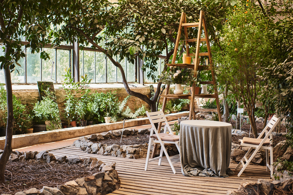piękne i nowoczesne wnętrze szklarni z drewnianym stolikiem, krzesłami ogrodowymi i okrągłym stołem - Zdjęcie, obraz