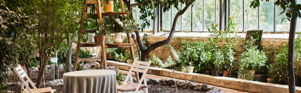 πανό του όμορφου και σύγχρονου εσωτερικού χώρου του θερμοκηπίου με ξύλινα rack, καρέκλες κήπου και στρογγυλό τραπέζι - Φωτογραφία, εικόνα