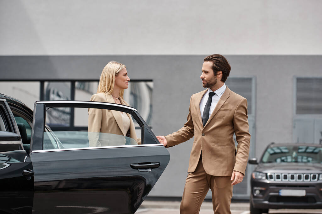 bearded elegant man and stylish blonde businesswoman holding hands near luxury car on city street - Photo, Image