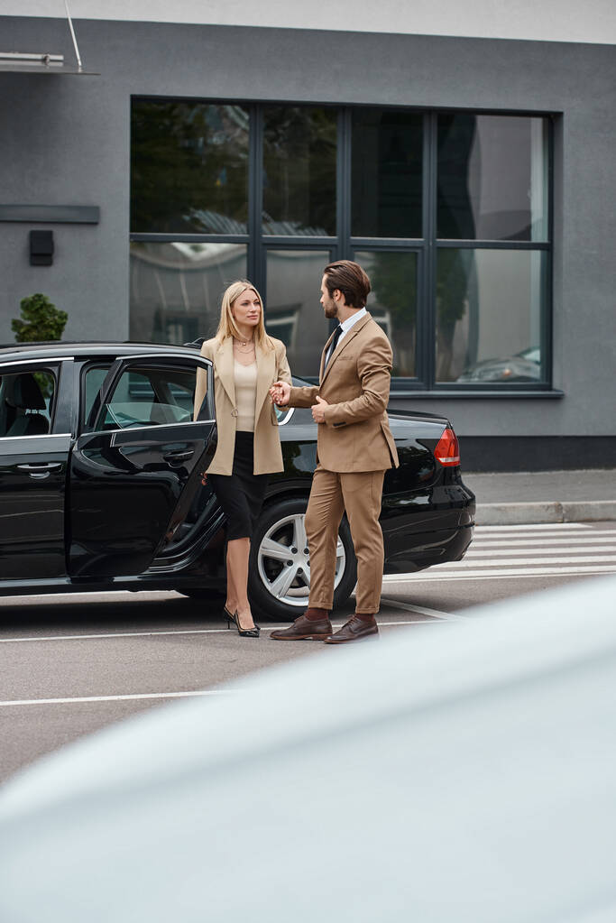 elegante pareja de negocios en formal desgaste de la mano y mirando unos a otros cerca de coche en la calle - Foto, imagen