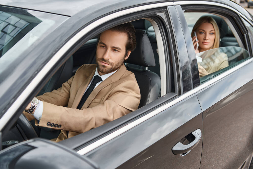 hombre guapo y elegante coche de conducción cerca de atractiva mujer de negocios rubia hablando en el teléfono inteligente - Foto, Imagen