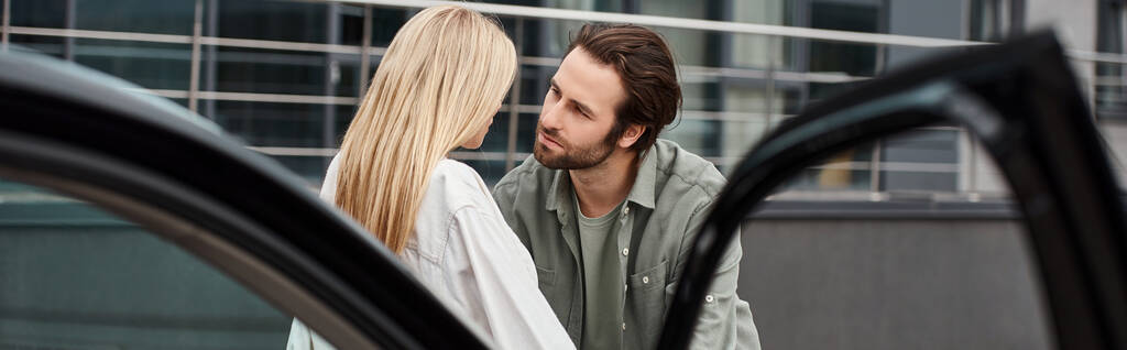 trendy man looking at stylish blonde woman near modern car on urban street, horizontal banner - Photo, Image